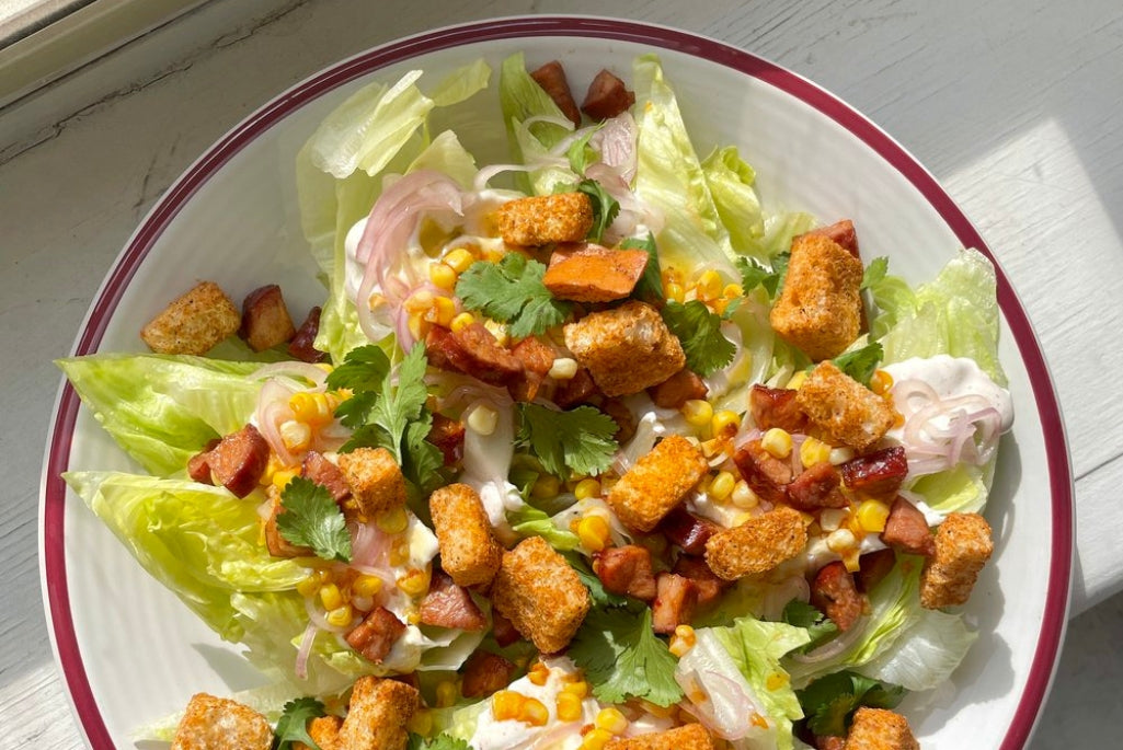 a salad of iceberg lettuce, croutons, onions and chorizo in a bowl on a windowsill.