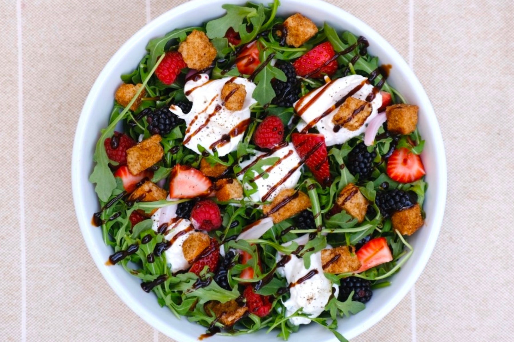 a berry burrata cheese salad with croutons and arugula on a tablecloth.