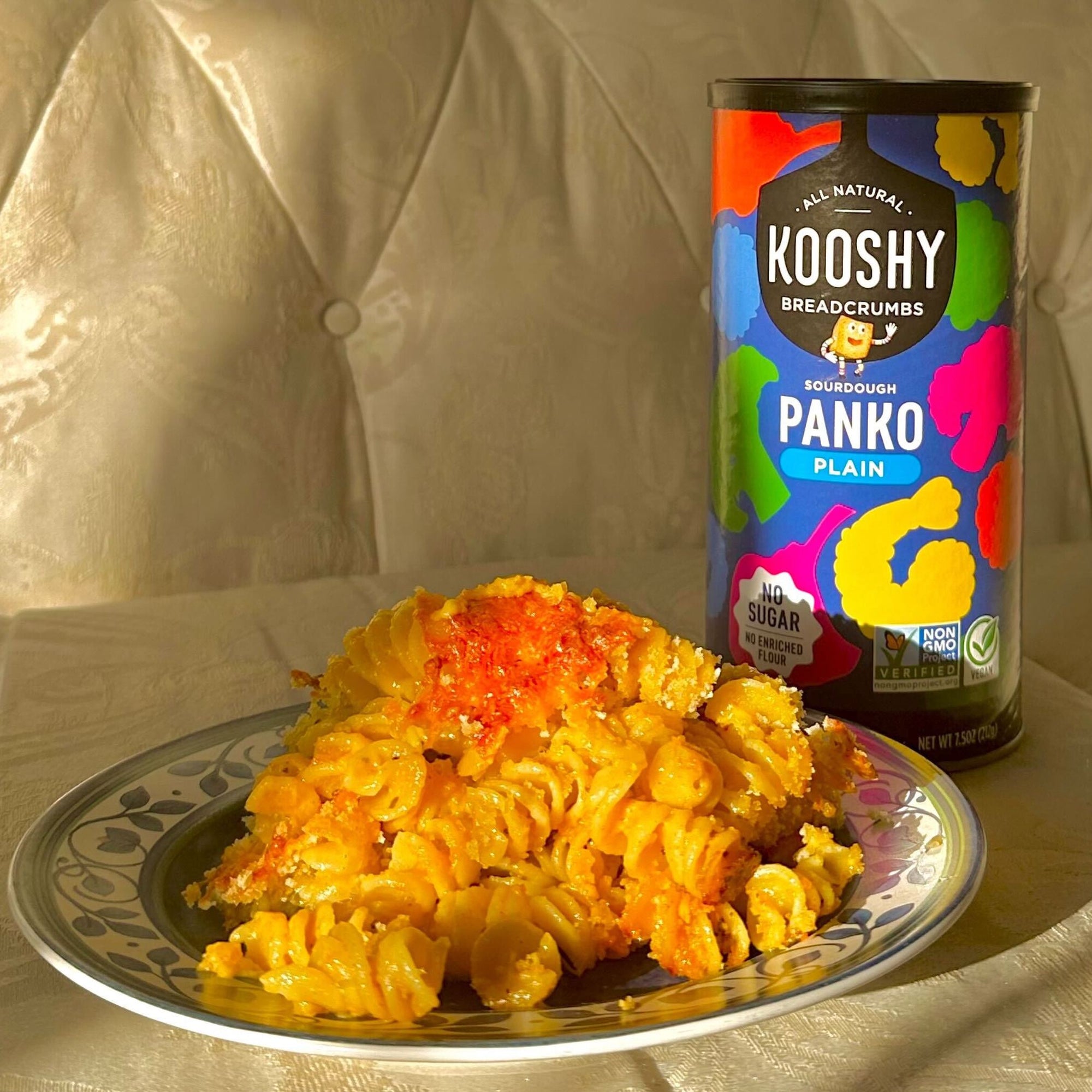 a plate of mac and cheese on a couch with a can of panko breadcrumbs.