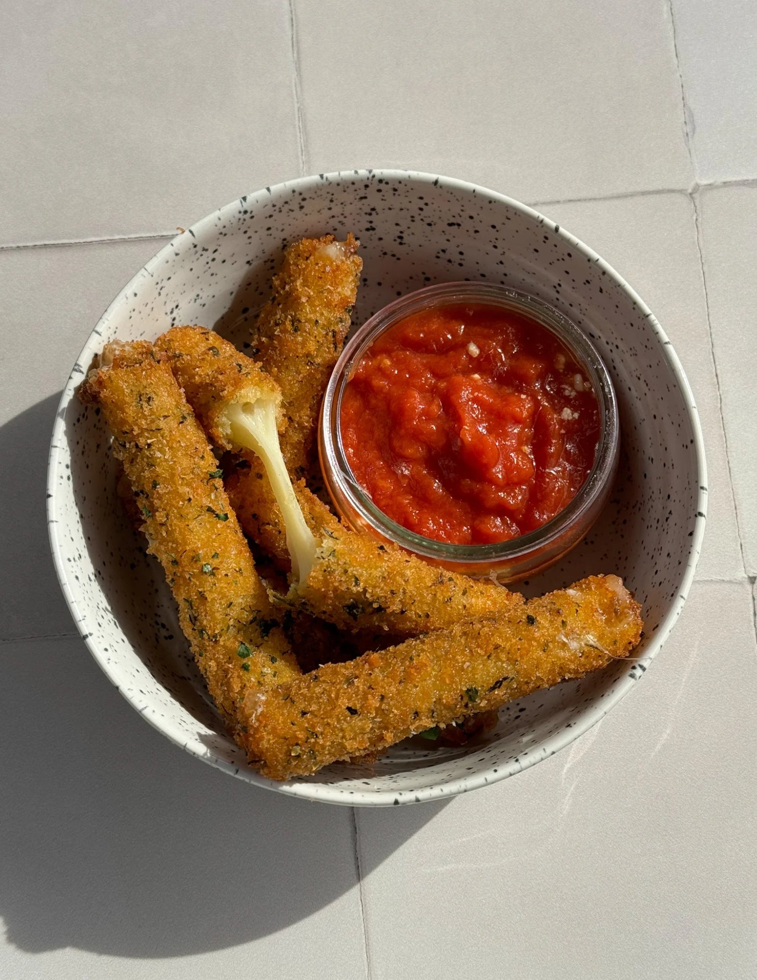mozzarella sticks in a bowl with tomato sauce on a white countertop.
