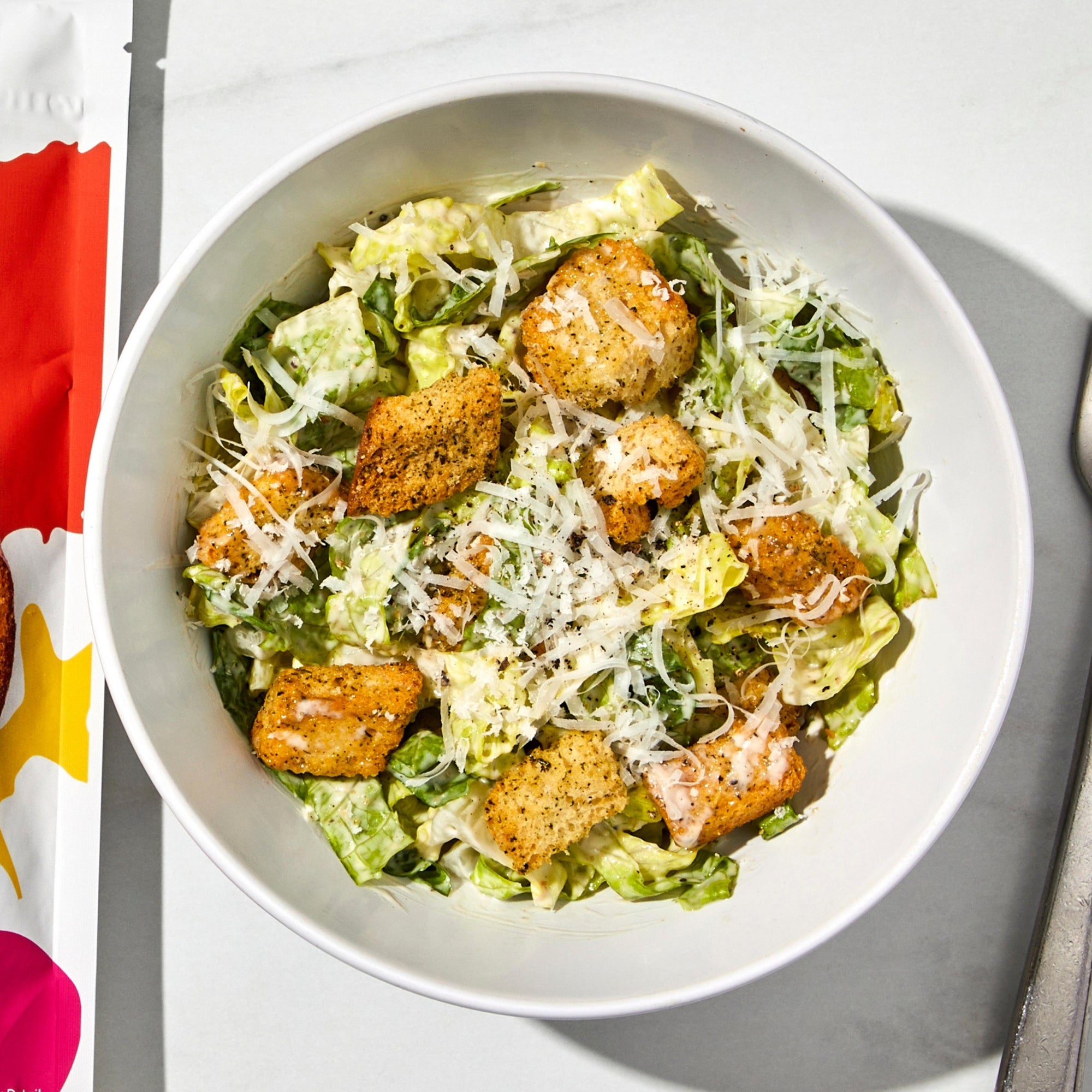 Bowl of caesar salad with Mambo Italiano flavor croutons and a silver fork.