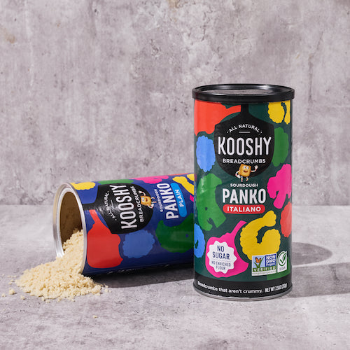 Packaging of both flavors of kooshy breadcrumbs with breadcrumbs pouring out of the plain can onto a marble table.