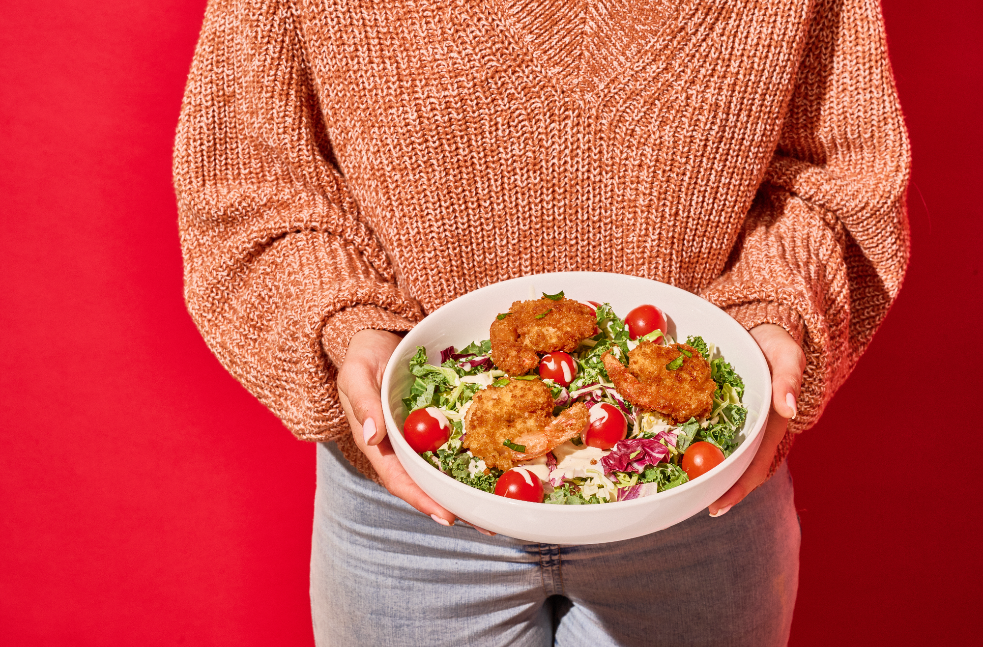 women wearing red sweater holding a bowl of crispy panko shrimp salad.