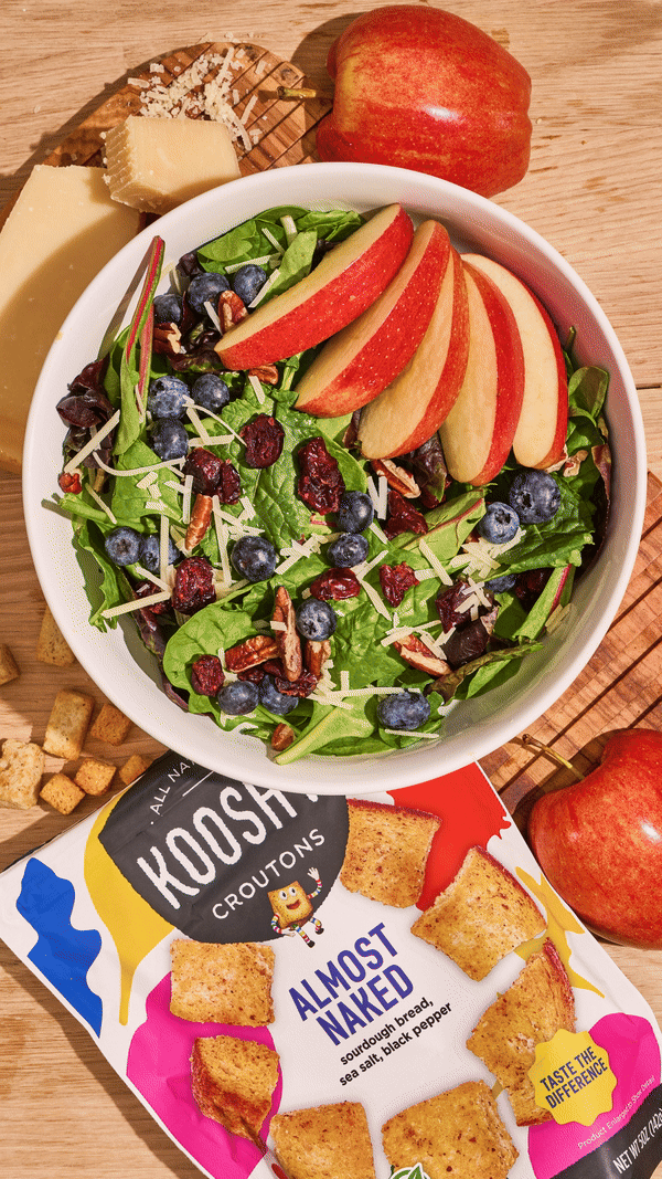 Salad containing apples and berries with croutons getting added to it.