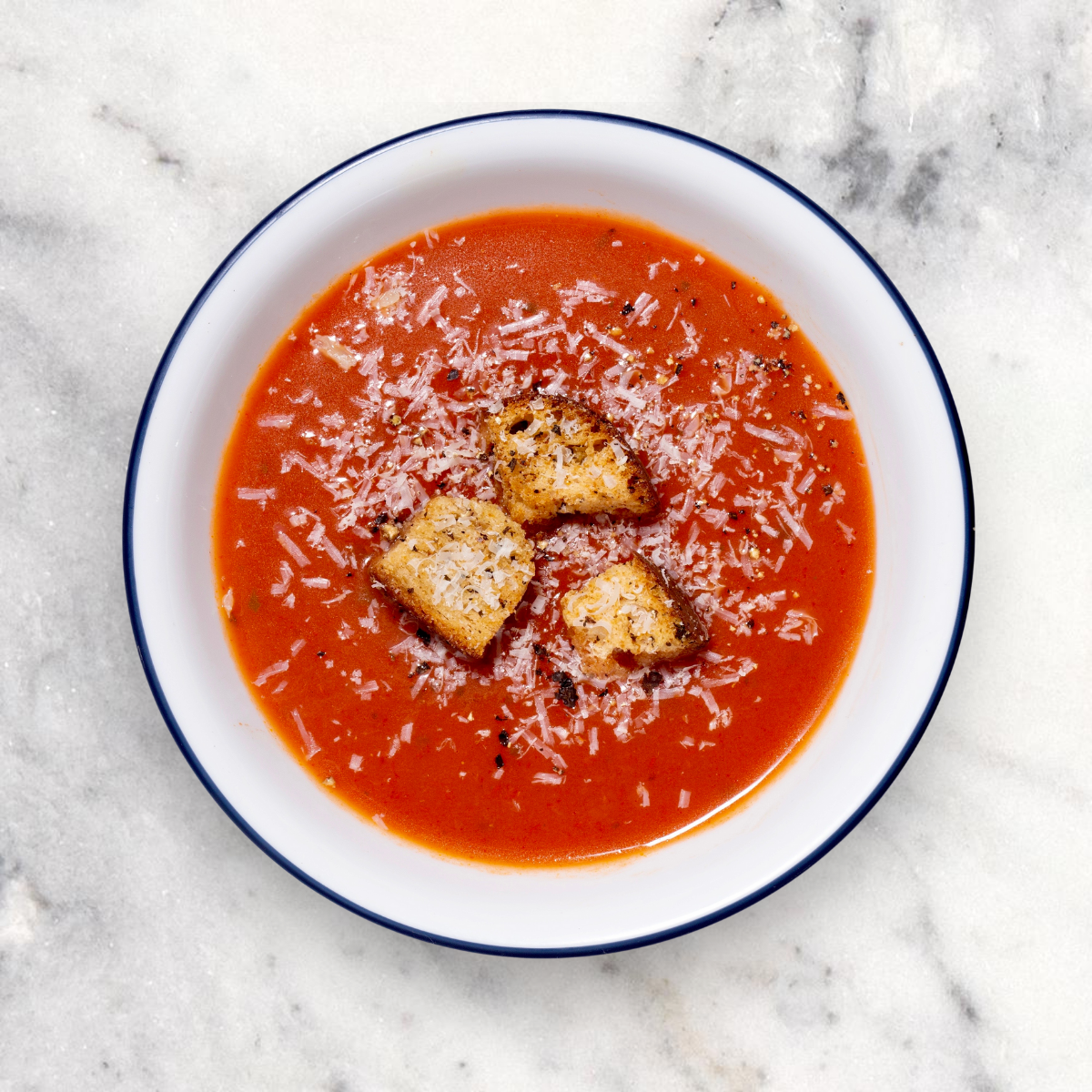 Bowl of tomato soup with croutons on a marble counter.