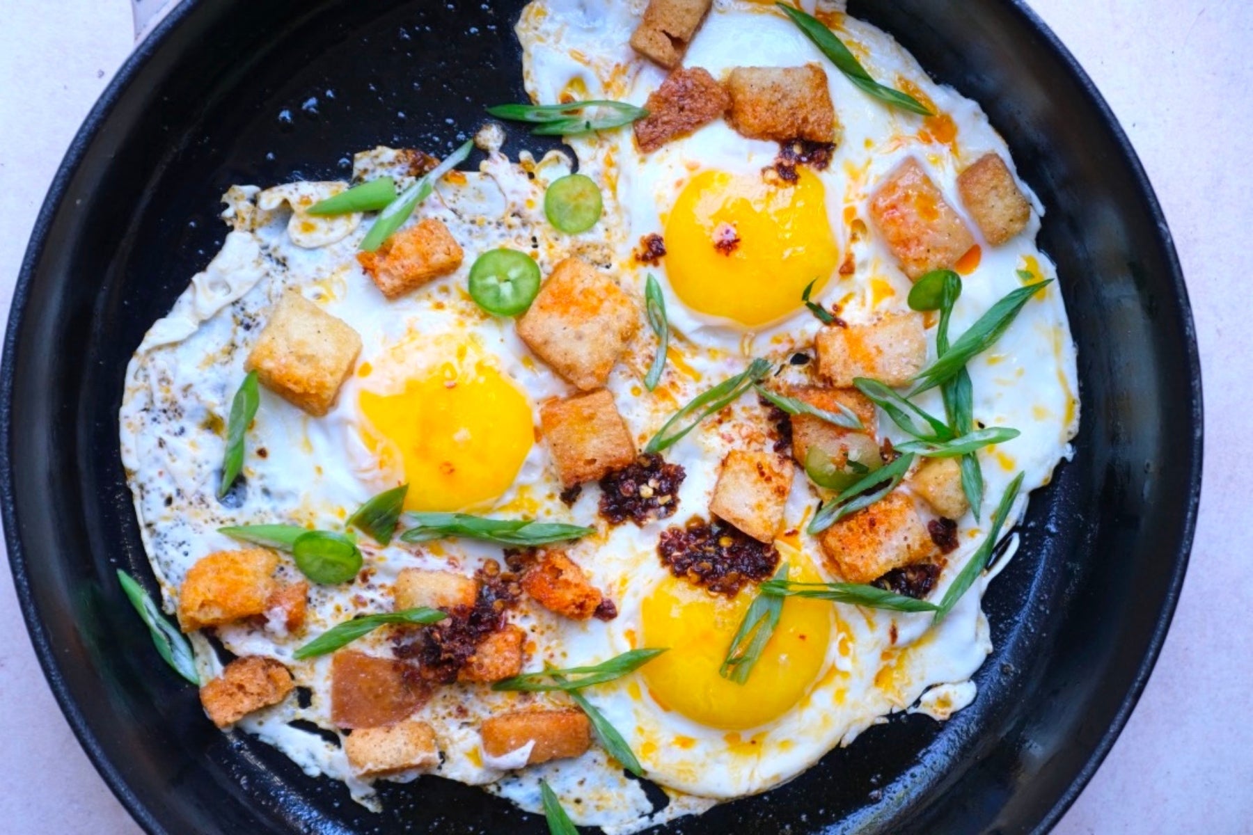 Fried eggs with croutons and sliced green onions in a black cast iron skillet.