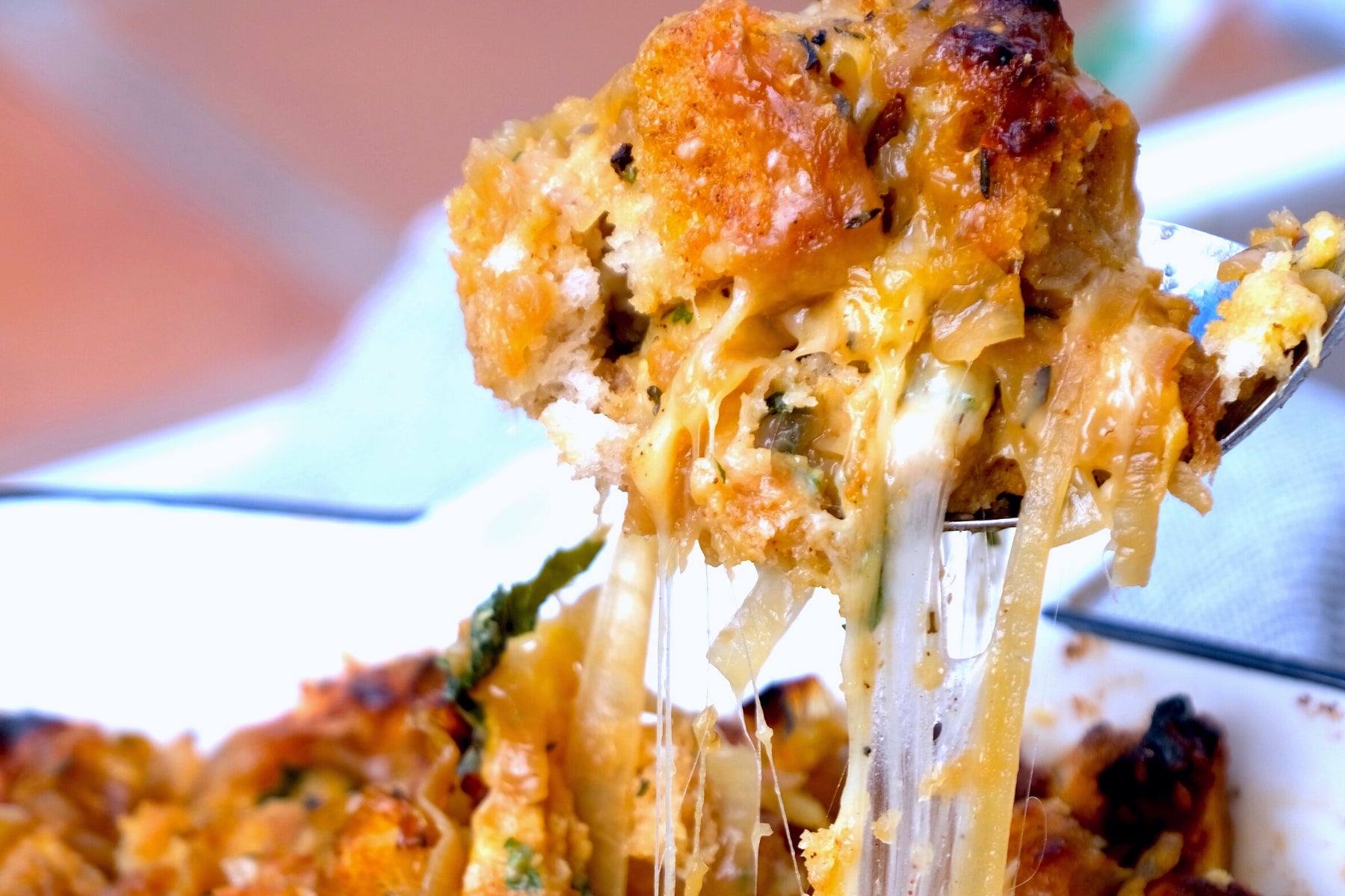 a silver spoon pulling french onion stuffing from a larger casserole dish with strings of melty cheese showing. 