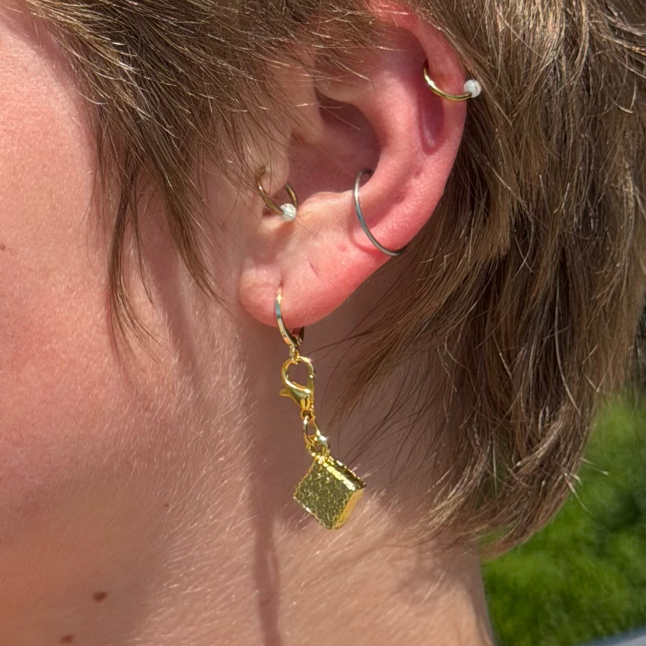 Close-up of an ear with gold earrings and a blurred background