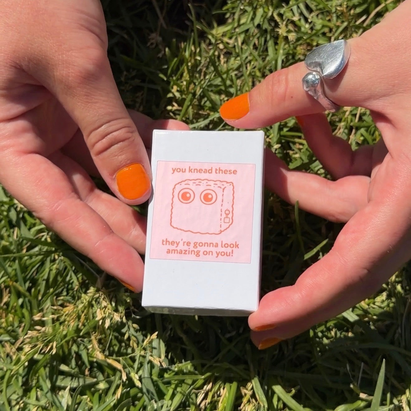 White box with pink label held by hands on grass