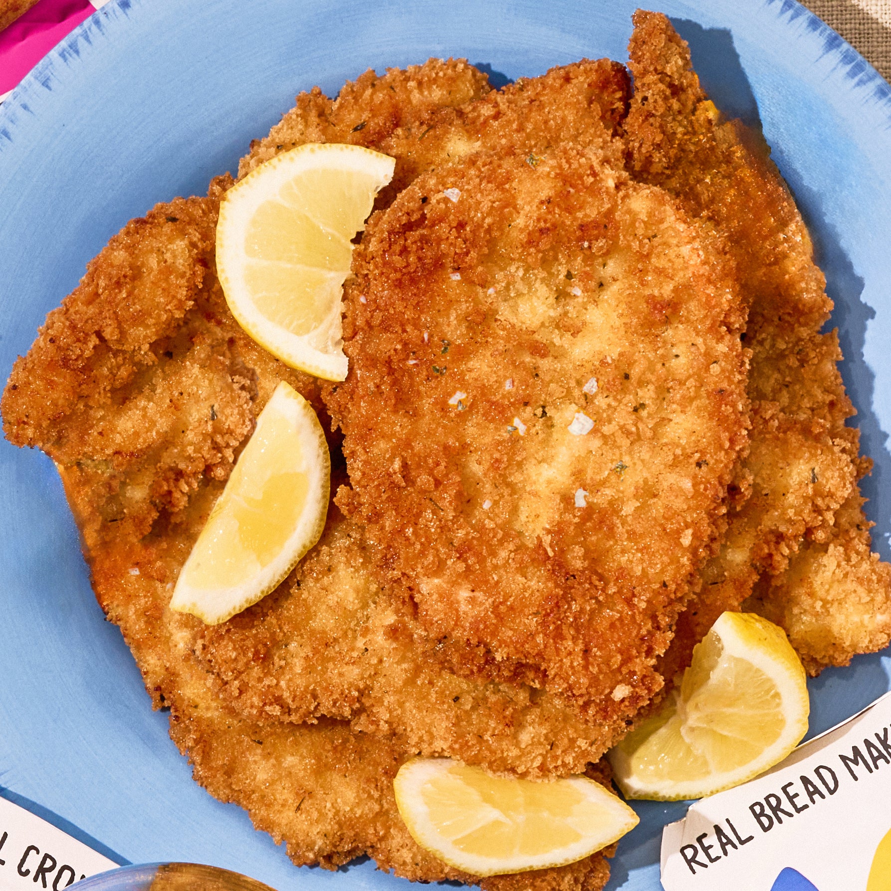 Crispy chicken cutlet with lemon wedges on a blue plate.
