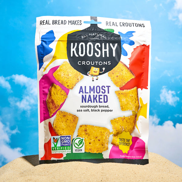 Almost Naked crouton bag on a beach with blue sky behind it.