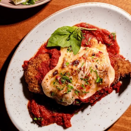 Chicken parm on a plate with tomato sauce and basil.